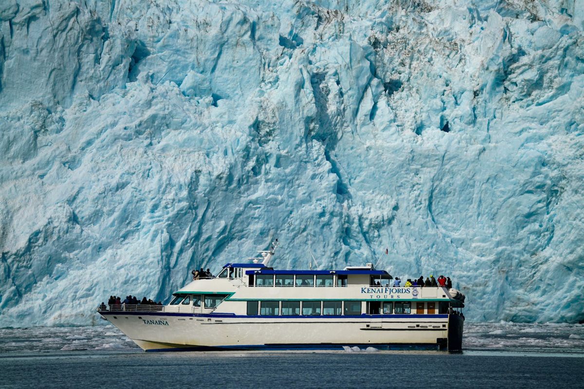 A day-tour boat beside the face of a huge blue tidewater glacier in Alaska