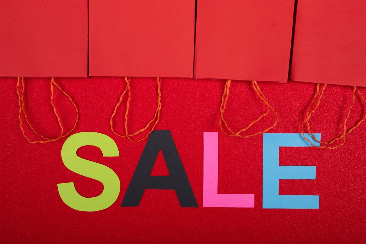 A colourful sale sign beside red shopping bags