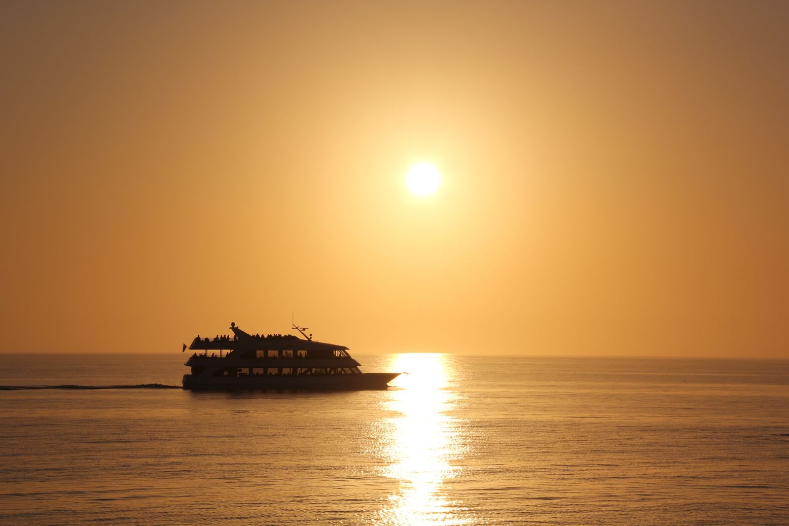A passenger boat in silhouette on a golden sunset sea, a reminder that the best time to book a cruise is planned well ahead