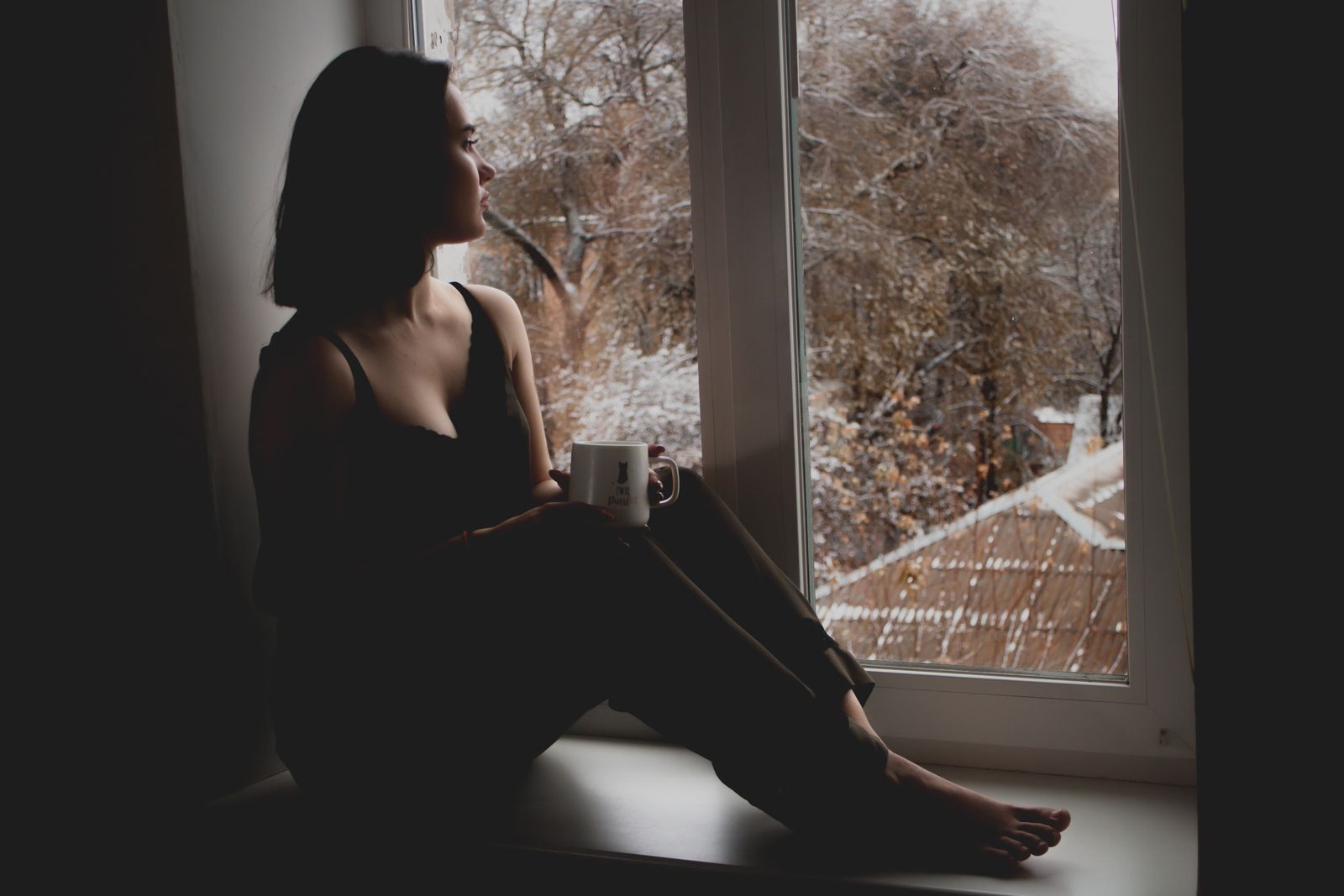 A woman with a warm drink by a window on a snowy day, the season of wave season cruise deals